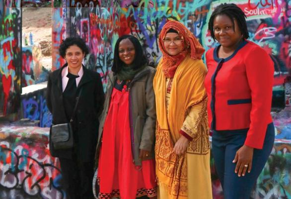 Women in a line against a wall of graffiti